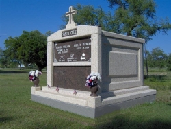 Four-space deluxe mausoleum with cross, fluted columns, turned vases on pedestals, step-up trim pieces on a foundation/slab in D’Iberville, MS