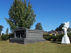 Side-by-side deluxe mausoleum deep gray with engraved inlays in the columns, vases on pedestals, step-up trim pieces on a foundation/slab in Taylorsville, MS