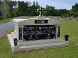 Side-by-side deluxe mausoleum with a cross, engraved granite inlays in the columns, vases on pedestals, step-up trim pieces on a foundation/slab in Mize, MS