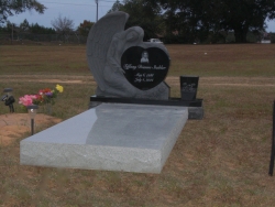 Single upright headstone with a large angel with heart and vase and granite ledger in Bayou LaBatre, AL