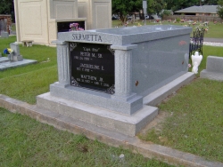 Single gray granite mausoleum with gable roof and fluted Roman columns on a foundation in Biloxi, MS